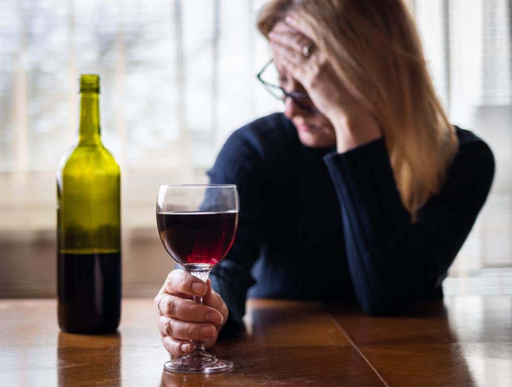 Lonely sad woman drinking red wine at home. Depression and sadness concept. Alcohol abuse social problem.