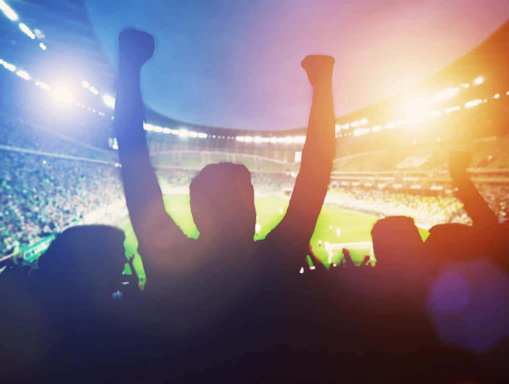 Happy football fans support their team and celebrating goal with hands up. Perhaps, they're listening to this best sports anthems list. Who's to say?