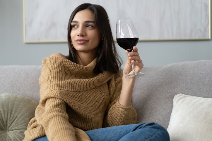 woman sitting on couch having raised glass with red wine in hand