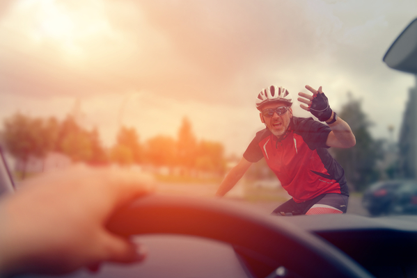 Cyclist on bike in front of car on roadway with hand up in the air