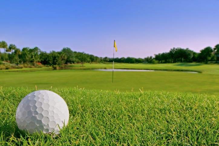 golf ball resting in dewy grass just above green on tropical course