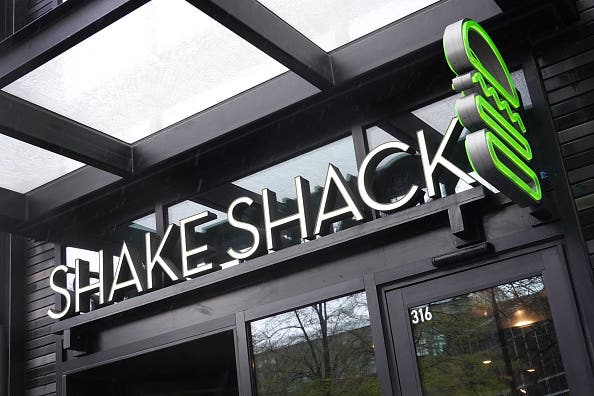 A sign hangs above a Shake Shack restaurant with logo.