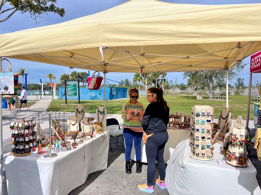 Tent outside on a sunny day. Underneath are two woman looking at handmade jewelry