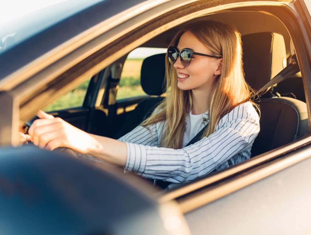 young happy smiling woman driving her new car at sunset