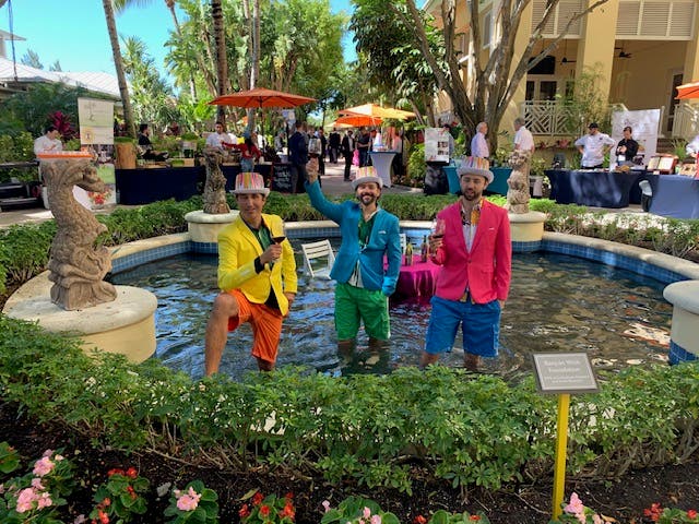 Three men in bright suits standing in a fountain. Ready for the Southwest Florida Food And Wine Fest