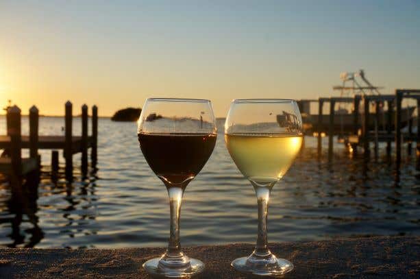 two wine glasses on a wooden rail at sunset over the water. One is full of red wine, the other has white wine perfect for Romantic Dining In Naples