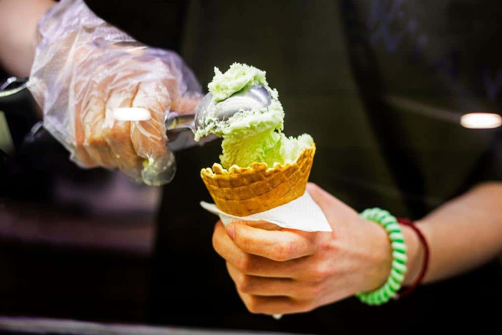 Scooping green ice cream into a waffle cone