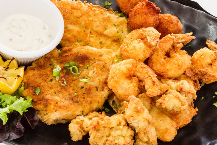 Fried seafood platter with fish, shrimp, oysters, hush puppies, and a crab cake.