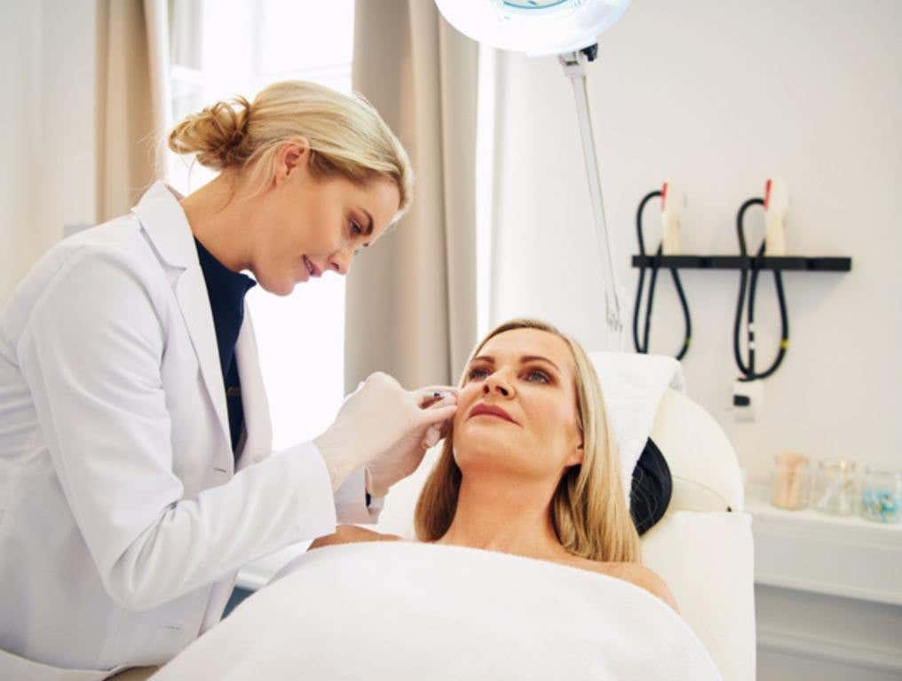 Young female doctor doing botox injections on the face of a mature woman lying on a table in a beauty clinic