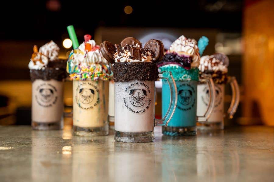 Row of milkshakes in a variety of colors with all kinds of toppings from donuts to Oreos and more. The New Mean Mugs Milkshake Bar