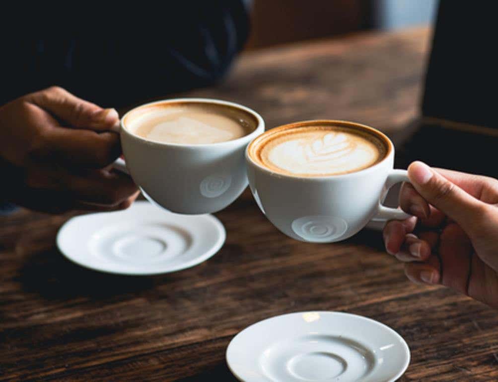 Close-up of a man and woman clinking a white coffee cup in a coffee shop. while talking at work