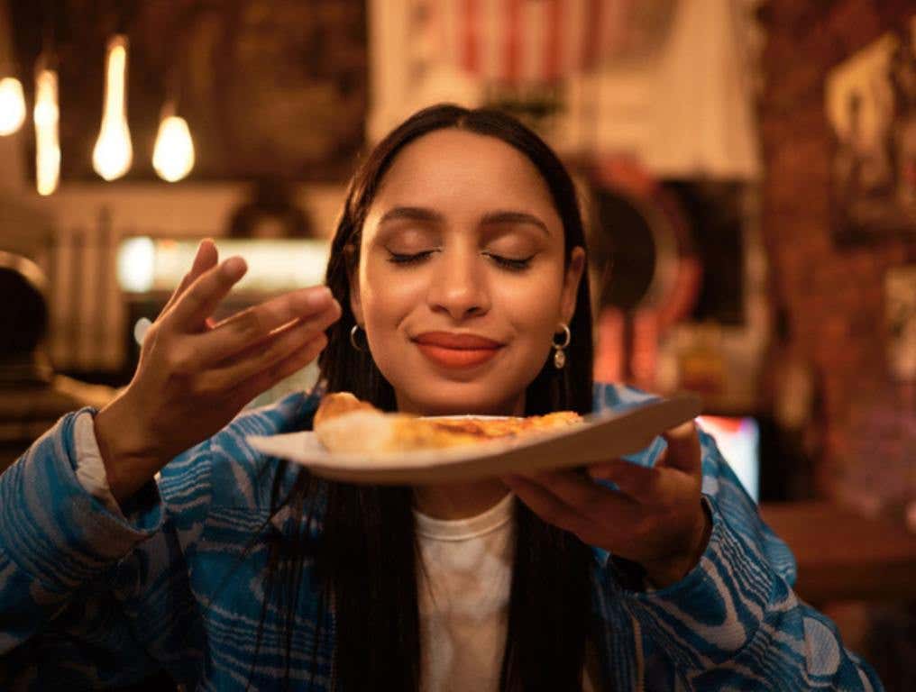 Hungry woman with delicious pizza, food or consumables at a bar, restaurant or diner at night. One happy and casual girl, foodie or tourist enjoying a dinner meal at a local trendy location, foodie