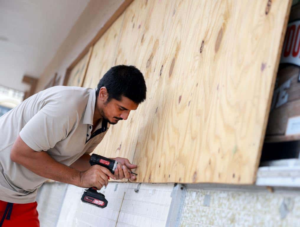 Sk Islam puts plywood over a store's windows before Hurricane Milton's arrival on October 08, 2024 in Naples, Florida.