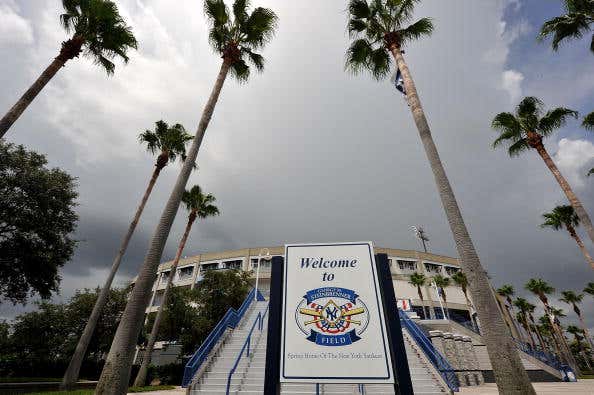 A sign welcoming fans to Steinbrenner field with the stadium in the background and palm trees.