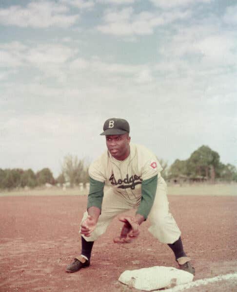 American professional baseball player Jackie Robinson (1919 - 1972) of the Brooklyn Dodgers, dressed in a road uniform, crouches by the base and prepares to catch a ball, 1951.