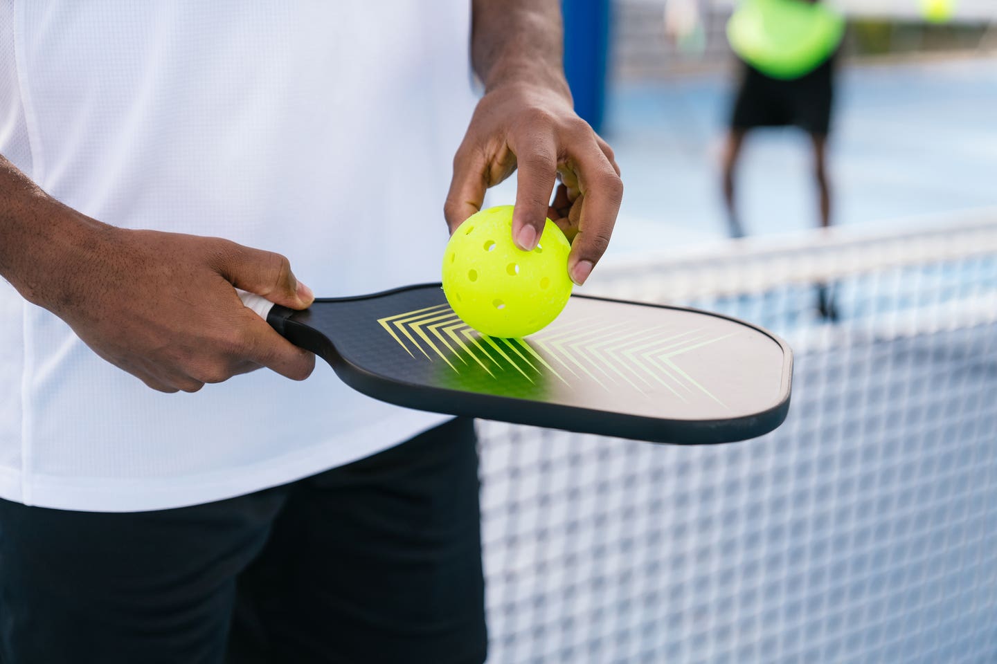 Close-up of a pickleball paddle and ball held by an African American player, ready for the game. Concept of equipment and readiness in pickleball.