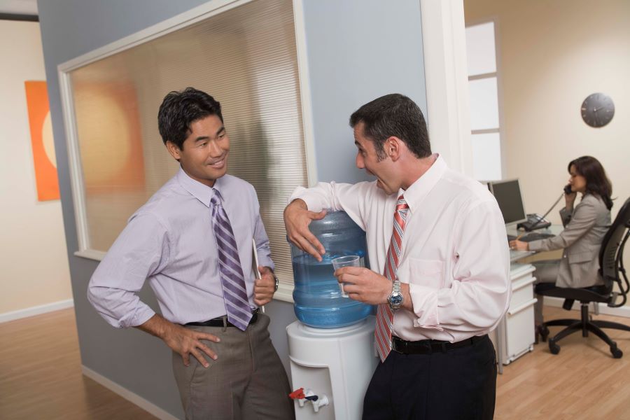 Two businessmen standing around a water cooler laughing 